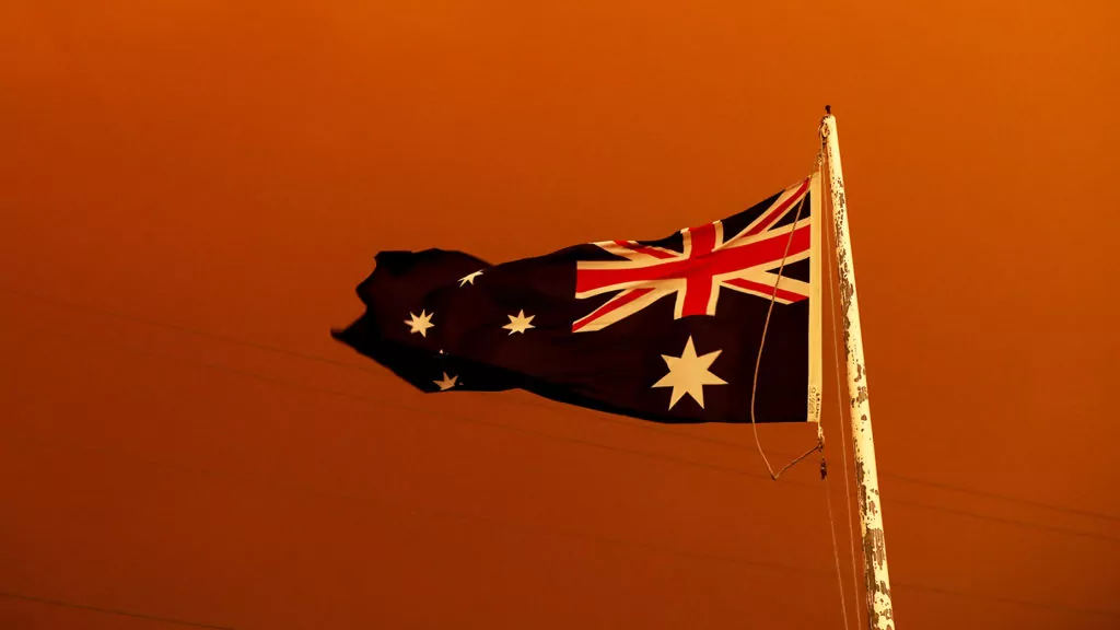 EAST GIPPSLAND, AUSTRALIA - JANUARY 04: The Australia Flag flies under red skies from the fires on January 04, 2020 in Bruthen Australia. Two people are dead and 28 remain missing following bushfires across the East Gippsland area, with Victorian premier Daniel Andrews declaring a state of disaster in the region. Thousands of people remain stranded in the coastal town of Mallacoota and are being evacuated by navy ships to Melbourne. (Photo by Darrian Traynor/Getty Images)